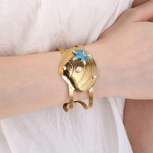 Macro detail of gold shell texture cuff with blue starfish and white pearls on wrist