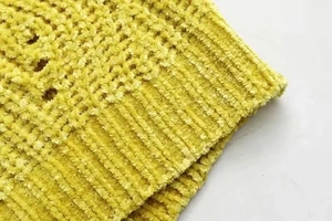 Detailed macro of yellow chenille knit texture with cable patterns and ribbed finish