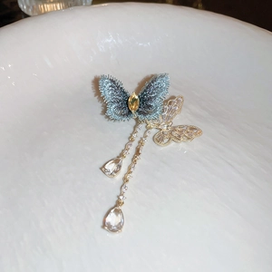 Macro detail of zircon butterfly brooch with blue fabric wings and gold tassel chains