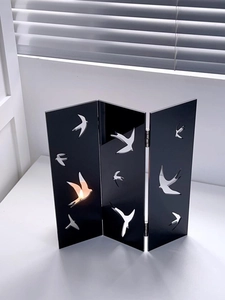 Detail of black acrylic folding screen with swallow cutouts and warm glowing light effect