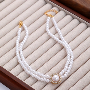 Détail d'un collier de perles à double rangée avec pendentif central doré serti de strass