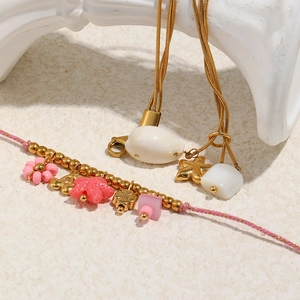 Goldene Muschel- und Seestern-Armbänder mit rosa geflochtenem Seil auf Steindeko