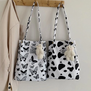 Detail view of canvas tote bags with cow print and bear charm on wooden hooks