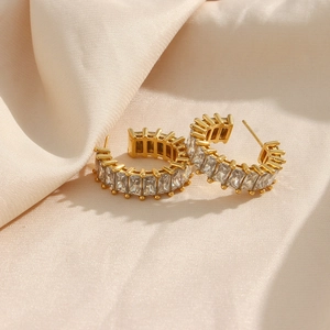 Vue macro de boucles d'oreilles C en or 18K avec zircons baguette sur soie champagne