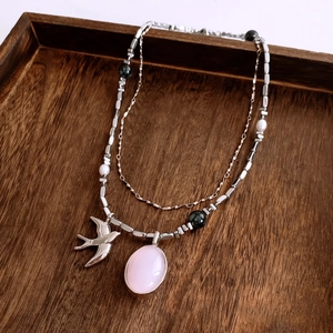 Gros plan du collier vintage oiseau avec pierre rose sur un plateau en bois