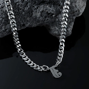 Detailed close-up of a silver Cuban chain necklace with letter F pendant on volcanic rock
