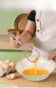 Close-up of a manual silicone whisk with colorful wires stirring eggs in a ceramic bowl