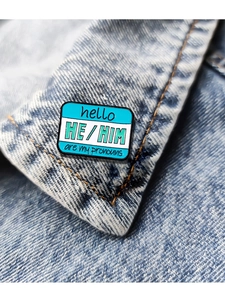 Detail of HE / HIM pronouns enamel pin pinned on a classic blue denim jacket lapel