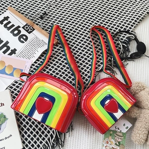 Flat lay of rainbow striped patent leather crossbody bags with red heart patch and strap