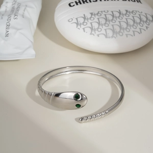 Detailed view of silver snake-shaped cuff bracelet featuring green stone eyes and texture