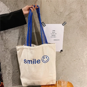 Detail of embroidered smile logo on off-white canvas tote bag with pompom shoulder strap