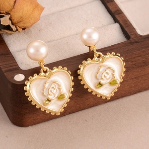 Detailed macro view of heart-shaped pearl earrings with gold embossed rose on wooden box