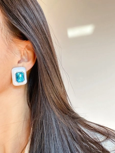 Close-up of model wearing blue rectangular gemstone earrings with white enamel finish
