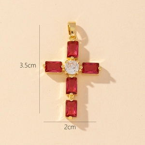 Detail view of a gold cross pendant with red gemstones and 3.5cm by 2cm dimensions
