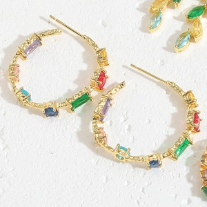 Macro view of gold hoop earrings with multi-colored crystals on a textured white surface