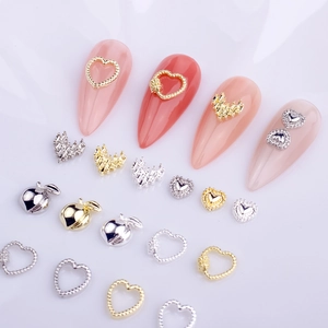 Macro view of hollow heart and mini metal alloy nail charms in gold and silver finish