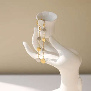 Detail of two-tone gold and silver circular disc tassel long drop earrings on display