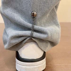 Close-up of denim pants hem with magnetic metal decorative buckle and chain detail