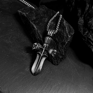 Detail of gothic silver dagger cross pendant with skull motif on dark stone background