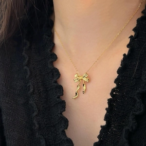 Detailed view of a textured gold bow necklace pendant on model with elegant lace top