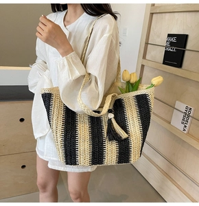 Detailed close-up of striped straw tote bag featuring decorative tassels and woven handles