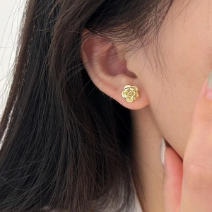 Close-up of a delicate gold rose stud earring worn on a model for a minimalist look