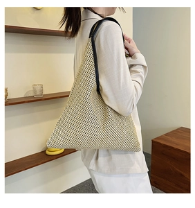 Model wearing a large beige woven tote bag with black straps in a minimalist studio