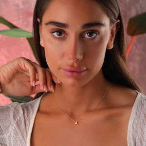 Polished gold initial A pendant on a thin metal chain worn by a model in soft light