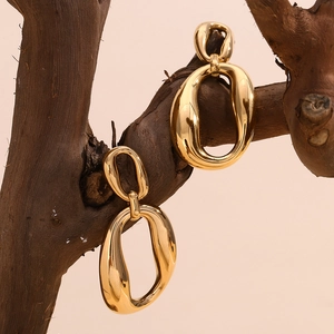 Macro detail of large gold oval hoop earrings hanging on a rustic dry wooden branch
