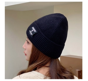 Detail of black ribbed knit beanie featuring an embroidered Moment of Ambitions label