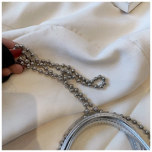 Detail of silver metallic mini bag featuring a sleek round handle and beaded chain strap