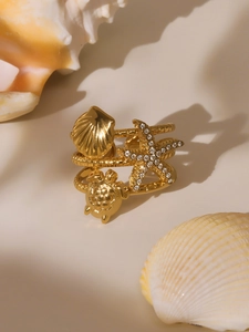 Close-up of gold nautical ring featuring starfish, sea turtle and shell charms with crystals
