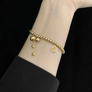 Close-up of golden beaded bracelet with Fu character tag and gourd charm on wrist