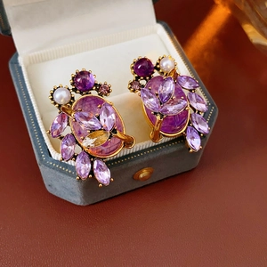 Detailed view of vintage gold earrings with purple crystals and pearls in a velvet box