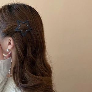 Detail of star-shaped black hair clip with white polka dots worn on brown hair