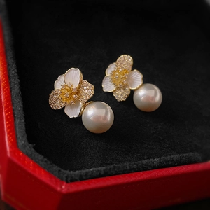 Macro detail of floral pearl earrings with gold plating and zircon inlay on red velvet