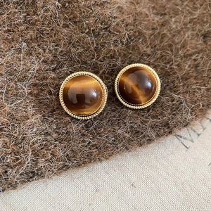 Macro detail of 18k gold plated round tiger eye stone stud earrings on brown wool fabric