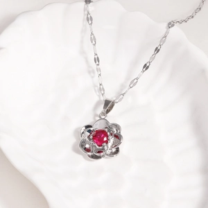 Silver flower pendant necklace with red gemstone on a white shell ceramic plate