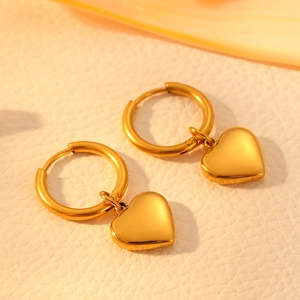 Close-up of golden stainless steel ball hoop earrings with solid heart pendants on leather