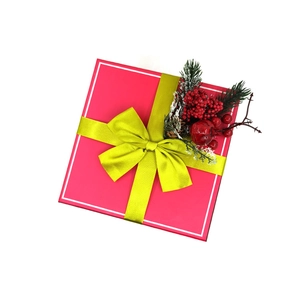 Dettaglio di una scatola regalo rosa con nastro verde lime e decorazioni natalizie con bacche