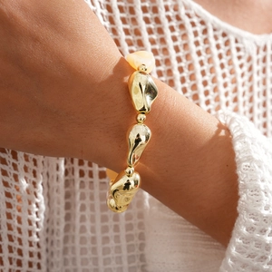 Détail d'un bracelet doré aux perles géométriques irrégulières porté au poignet