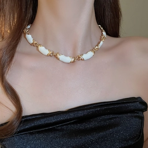 Gros plan sur le collier vintage en émail blanc avec liens X dorés sur le cou