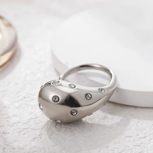 Detailed view of silver dome ring with inlaid crystals on a white textured surface
