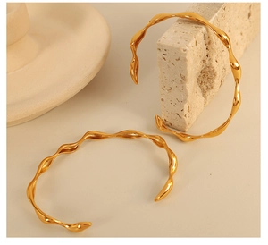 Macro shot of 18K gold plated wavy bangle featuring a polished fluid geometric texture