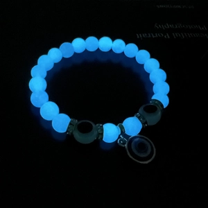 Luminous evil eye bracelet with blue glowing beads and metal pendant in dark background