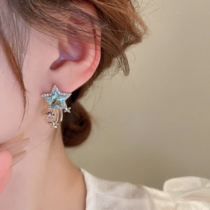 Close-up of star-shaped silver earring with blue zircon and elegant tassel drop