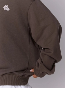 Détail du sweat marron ample avec poignets côtelés et logo Me & Me imprimé au dos