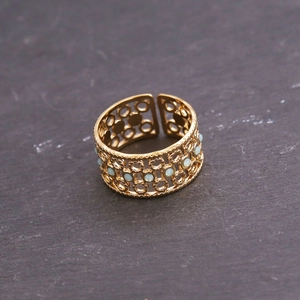 Gros plan détaillé d'une bague ajourée dorée avec des perles bleu clair sur roche sombre