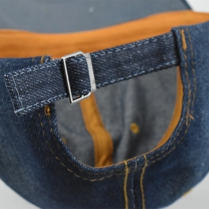 Detail of adjustable metal buckle on dark blue denim baseball cap with orange lining