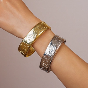 Detailed view of wide metal bangles in gold and silver with embossed scroll patterns